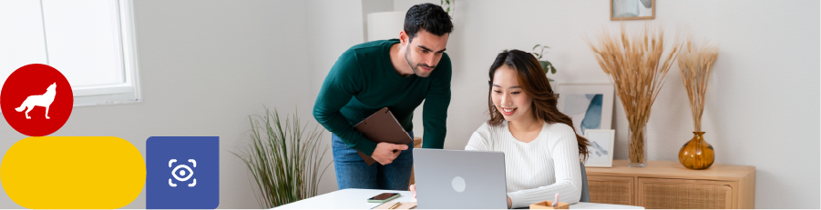 Two individuals collaborating, one seated with a laptop and another standing with a tablet in a modern office.

